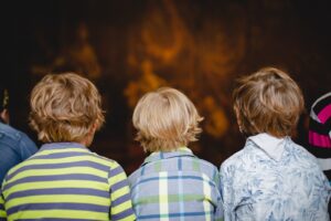 Kolorowa fotografia przedstawia trójkę dzieci siedzących tyłem do fotografa i słuchających wykładu w muzeum.